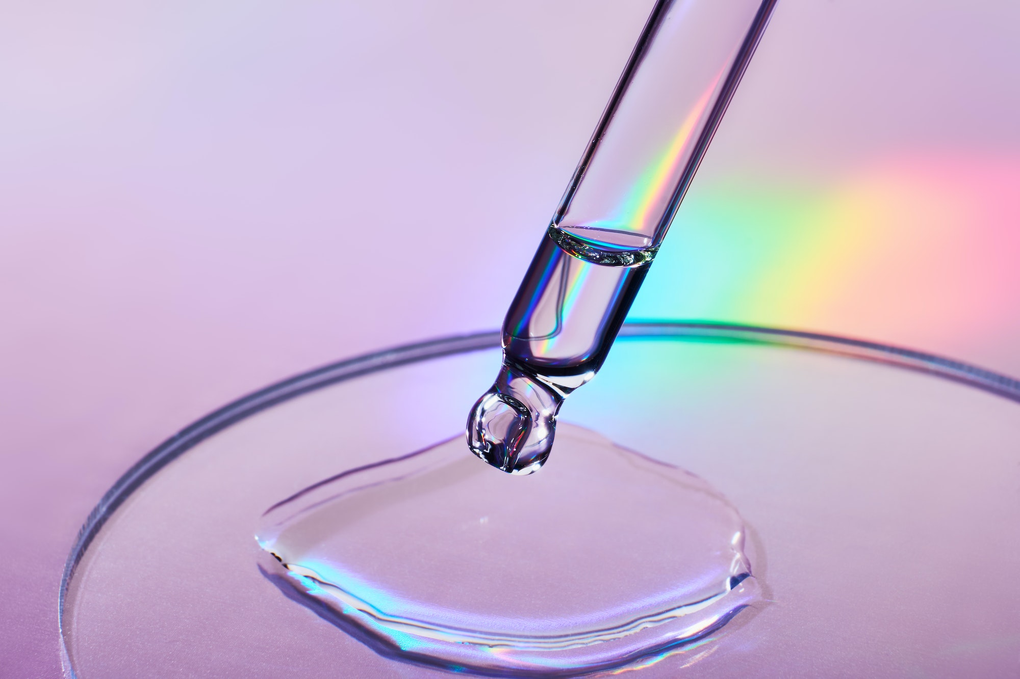 Pipette with sample of cosmetic product in petri dish on holographic background